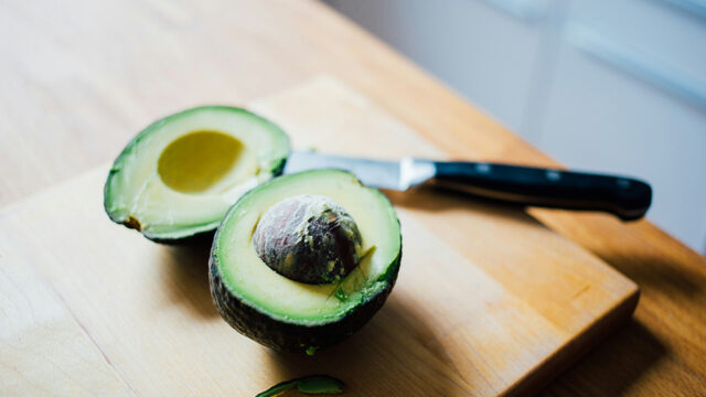 Halbierte Avocado auf einem Brett mit einem Messer