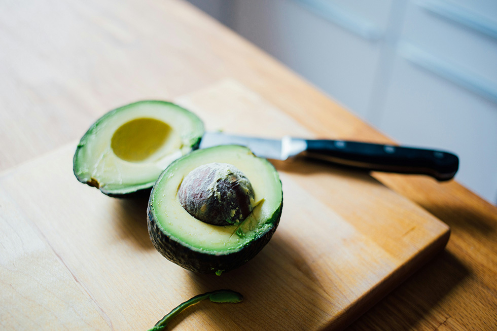 Halbierte Avocado auf einem Brett mit einem Messer