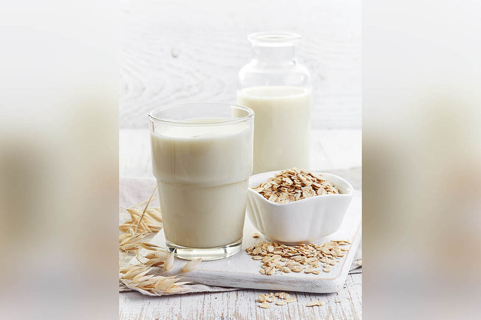 Glass of oat milk on white wooden background