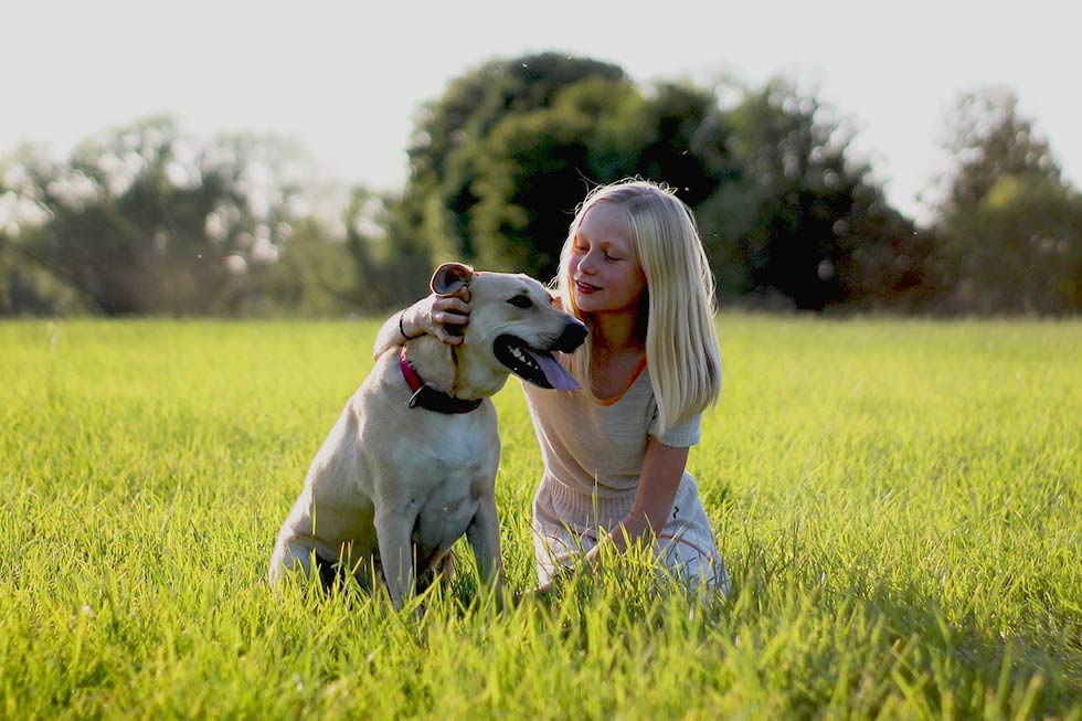 Maedchen sitzt mit Hund auf einer Wiese