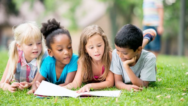 Kinder lesen Buecher auf einer Wiese.