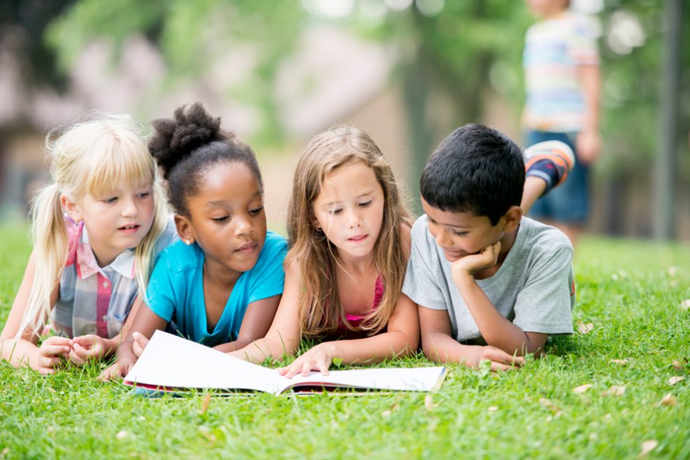 Kinder lesen Buecher auf einer Wiese.