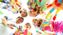 Kinder mit bunt bemalten Haenden stehen im Kreis.