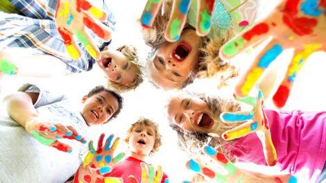 Kinder mit bunt bemalten Haenden stehen im Kreis.