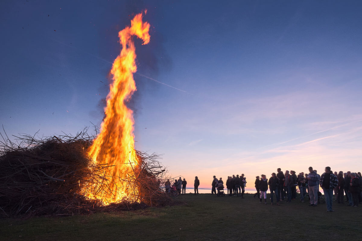 Osterfeuer mit großem Lagerfeuer vor Sonnenuntergang und Menschenmenge im Hintergrund